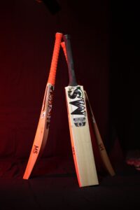 Three wooden cricket bats standing on red background studio lighting