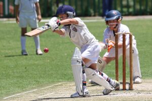 A professional cricket batsman wearing a helmet swinging a wooden bat during an international match