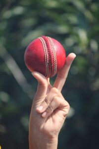 A close-up view of a professional cricket player's fingers gripping a red leather ball along the vertical seam.