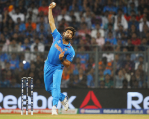 A professional cricket bowler in mid-action delivery on a green turf pitch during a stadium match.