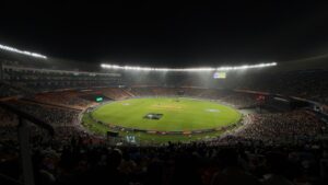 A massive modern cricket stadium flooded under bright stadium lights with a green pitch, representing famous cricket tournaments and international championships.