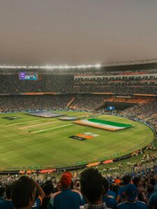 A wide panoramic view of a packed international cricket stadium under bright floodlights during a night match.